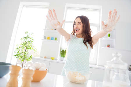 Portrait of cheerful funky girl housewife have bakery morning prepare dough show hands flour wear white apron in kitchen houseの写真素材