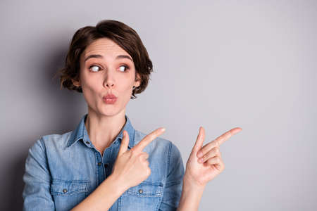 Closeup photo of attractive funny lady wavy hairdo direct fingers side empty space showing nice offer wondered send kiss wear casual denim shirt isolated grey color backgroundの写真素材