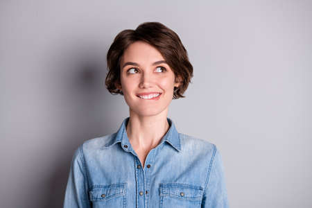 Closeup photo of cheerful funny lady wavy bobbed hairdo smiling biting white teeth look side empty space interested wear casual denim shirt isolated grey color backgroundの写真素材