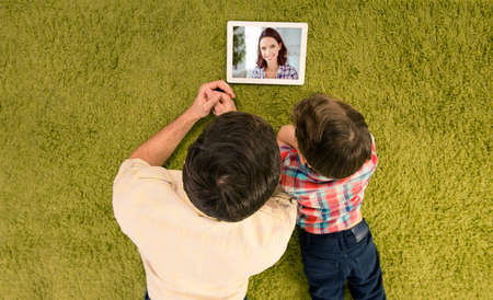 Top above high angle view of happy smiling father and small son lying on green carpet talking to mom...