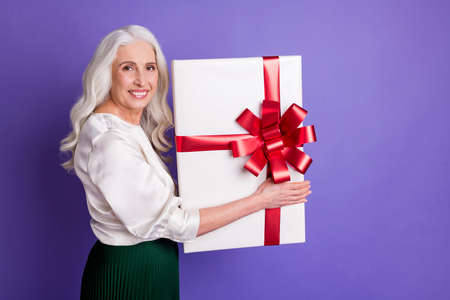 Profile side photo of cheerful content old woman lovely granny hold big package gift box she get from her family wear good look outfit isolated over vibrant color backgroundの写真素材