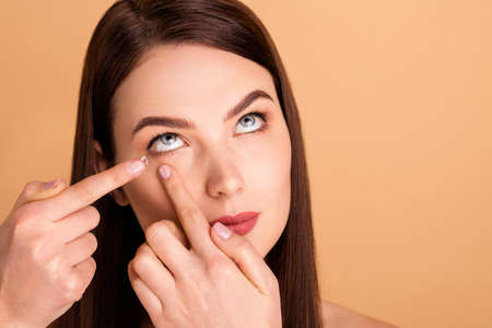 Close up photo of focused girlish glamorous girl use lens prescribed by doctor oculist to cure myopia become beauty isolated over beige color backgroundの写真素材