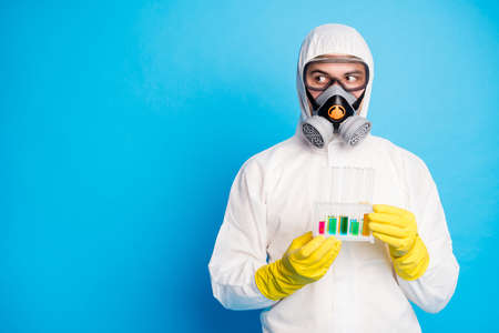 Portrait of chemist man hold test-tube ncov vaccination look copyspace wear white suit hazmat yellow latex gloves goggles isolated blue color backgroundの写真素材