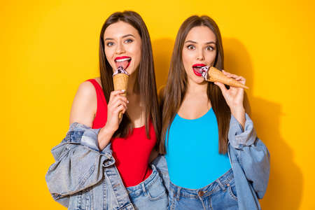 Portrait of positive cheerful charming girls youngsters eat delicious icecream scoops waffle cone wear bright red singlet isolated over shine color backgroundの写真素材