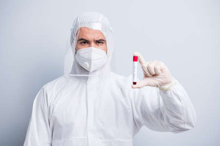 Photo of serious guy expert virology center clinic hold patient blood probe covid result wear face mask hood uniform suit plastic facial protection eyes nose isolated grey color backgroundの写真素材