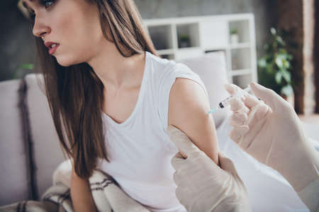 Cropped photo of young sick ill patient lady sit sofa unwell call emergency doc virologist flu cold covid injection hand shoulder medication help wear latex gloves protective uniform indoorsの写真素材