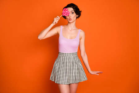 Portrait of funky sweet lovely teen girl hold lollipop close cover eyes send air kiss enjoy free time wear tank-top checkered outfit isolated over bright shine color backgroundの写真素材