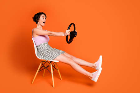 Full length profile side photo astonished positive girl sit chair hold steering wheel imagine she drive fast automobile wear checkered pink singlet isolated bright shine color backgroundの写真素材