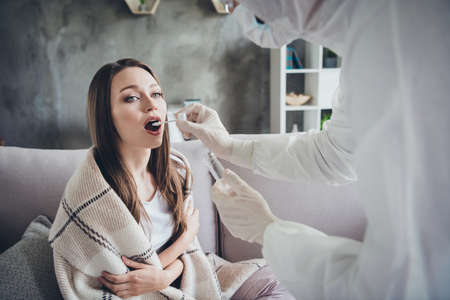 Photo of lonely patient lady alone sit sofa feel unwell call ambulance service guy doc virologist collect saliva probe corona virus bacteria wear uniform protection visit her flat indoorsの写真素材