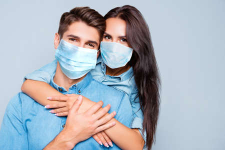 Portrait of happy cute lovers embracing on gray background, wear medical safety sterile mask on face, social distance pandemic corona virus prevention protection concept covid 19の写真素材