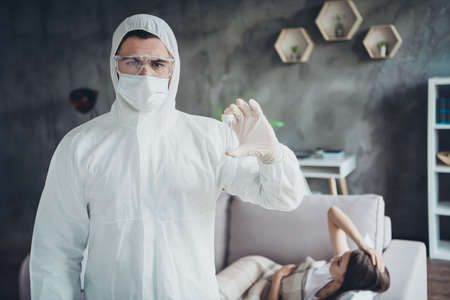 Photo of young sick patient lady lying resting sofa unwell call ambulance guy doc virologist examination collected saliva probe flu cold covid test wear uniform protection visit flat indoorsの写真素材