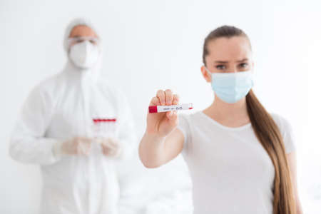 Photo of sick patient student lady unwell call emergency doc virologist collected blood probe hold test tube positive negative covid result wear mask protective uniform bedroom indoorsの写真素材
