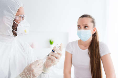 Closeup photo of young patient student lady feel unwell emergency doc virologist prepare antibiotic injection vaccine medication wear latex gloves protective uniform bedroom indoorsの写真素材