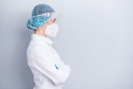 Profile photo of virologist doctor lady arms crossed nurse surgeon watch intern working process wear medical coat mask facial plastic protection shield surgical cap isolated grey backgroundの写真素材