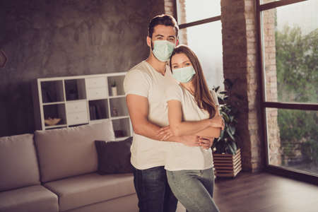 Photo of young couple lady guy spend quarantine isolation together stay home hugging piggyback happy emotions stand cosy cozy wear facial medical mask living room evening sun indoorsの写真素材