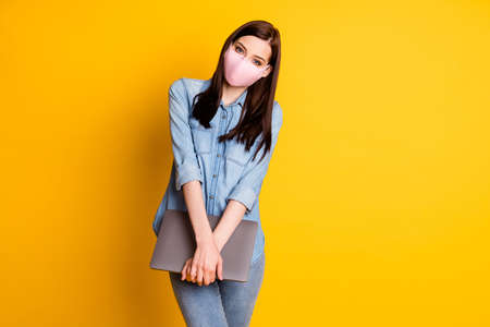 Portrait of positive girl in medical mask hold laptop enjoy working remote wear casual denim jeans shirt isolated over bright shine color backgroundの写真素材