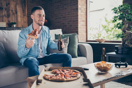 Profile photo of domestic handsome guy stay home good mood quarantine, time watch television eat pizza drink beer sit cozy sofa football season modern interior living room indoorsの写真素材