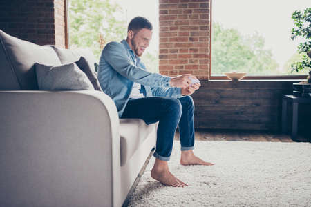 Profile photo of handsome guy stay home quarantine time hold telephone hands playing online video game trying hard addicted sit comfy sofa modern interior living room indoorsの写真素材