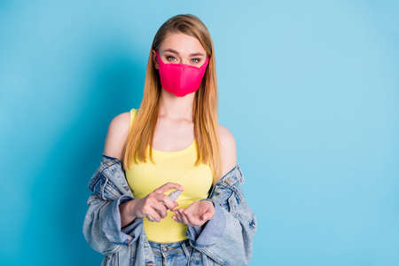 Photo of beautiful lady use little purse organizer antiseptic spray disinfecting arms after crowd social place wear face mask denim blazer yellow tank top isolated blue color backgroundの写真素材