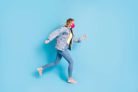 Full size profile photo of pretty lady quarantine finished run street outdoors jump high good mood shopping center direction wear face mask blazer jeans shoes isolated blue color backgroundの写真素材