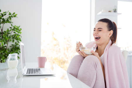 Profile photo of pretty homey housewife lady cozy sit morning kitchen covered blanket notebook watch movie have breakfast eat corn flakes laughing stay home quarantine indoorsの写真素材