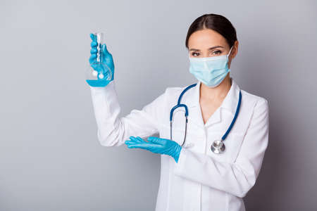 Photo of virologist doc lady experienced professional hold test flask tube examining vaccine showing project wear gloves facial mask uniform lab coat stethoscope isolated grey backgroundの写真素材