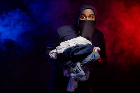 Portrait of scared frightened afro american guy rob boutique shop hold pile messy clothes horrified...
