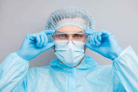 Closeup photo of guy expert doc virology center clinic hold arms on protective glasses wear gloves mask hazmat blue uniform suit plastic facial goggles isolated grey color backgroundの写真素材