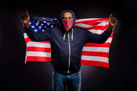 Photo of crazy furious angry rebellion revolt afro american guy hold us flag protest race discrimination wear sweater red bandanna jeans isolated over black color backgroundの写真素材