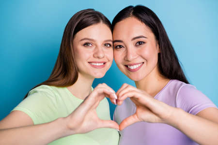 Closeup photo of two affectionate lesbians couple ladies romance date make arms fingers heart shape lovers celebrate anniversary wear casual t-shirts isolated blue color backgroundの写真素材