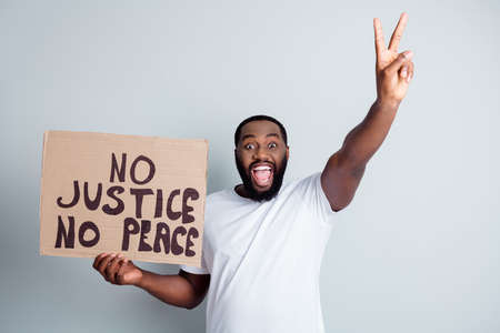 No justice no peace. Photo of cheerful dark skin afroamerican protester hold placard against black citizens lawlessness concept show v-sign positive attitude isolated grey color backgroundの写真素材