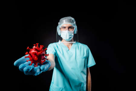 Closeup photo of guy doc virologist present whole world covid bacteria vaccine hold on open hand wear mask blue uniform surgical cap facial shield isolated black color backgroundの写真素材