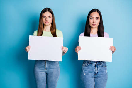 Photo of serious two people ladies lesbians couple hold arms white posters support same sex marriages express protest wear casual green violet t-shirts jeans isolated blue color backgroundの写真素材