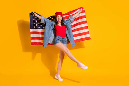 Full length photo of fit cheerful energetic street style girl youngster hold usa flag enjoy fourth july celebration wear red headwear jeans tank-top isolated over shine bright color backgroundの写真素材