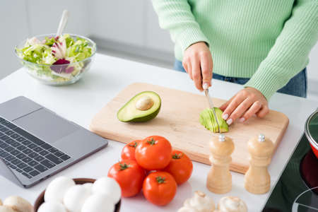 Cropped photo of housewife hold knife cutting fresh avocado mixing salad ingredients cooking tasty vegan meal look online recipe stand kitchen indoors casual clothingの写真素材