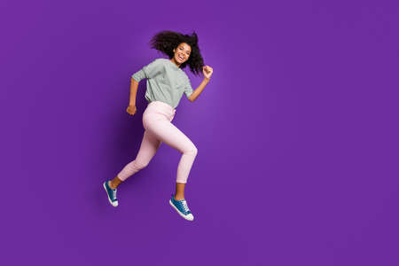 Full body photo of cheerful afro american girl jump run hurry fast after black friday discounts wear casual style outfit pants isolated over violet color backgroundの写真素材