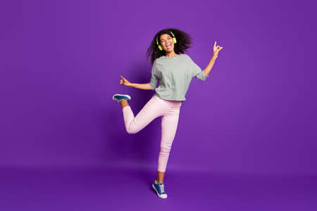 Full size photo of crazy cheerful teenager afro american girl listen song use headset sing dance feel rejoice scream wear striped shirt pink pants trousers isolated over purple color backgroundの写真素材