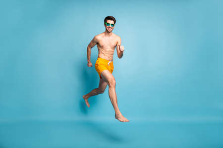 Full length body size view of his he nice attractive cheerful cheery guy in swimming shorts jumping running action motion isolated on bright vivid shine vibrant green blue turquoise color backgroundの写真素材
