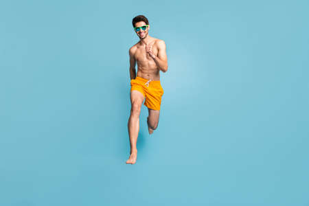 Full length body size view of his he nice attractive cheerful purposeful guy in swimming shorts jumping having fun running isolated on bright vivid shine vibrant green blue turquoise color backgroundの写真素材