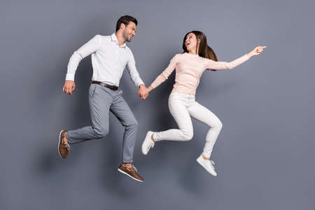 Full size profile photo pretty lady show finger handsome guy sales leading him running shopping center mall together addicted shoppers wear shirts pants shoes isolated grey color backgroundの写真素材