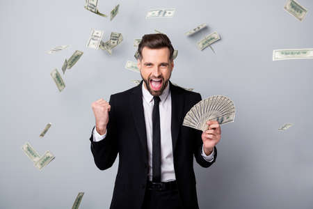 Ecstatic crazy man employee get debit salary millionaire lottery winner hold 100 hundred dollar fan money fly fall raise fists scream wear black blazer jacket isolated grey color backgroundの写真素材