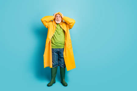 Full length body size view of his he nice overwhelmed grey-haired man fisherman wearing yellow plastic topcoat disaster cyclone reaction isolated on bright vivid shine vibrant blue color backgroundの写真素材