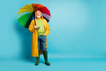 Full length body size view of his he nice cheerful cheery glad grey-haired man wearing, yellow plastic overcoat parasol rainy day isolated over bright vivid shine vibrant blue color backgroundの写真素材