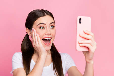 Closeup photo of pretty cheerful lady hold telephone hands excited emotions read positive comments arm on cheek wear casual white t-shirt isolated pastel pink color backgroundの写真素材