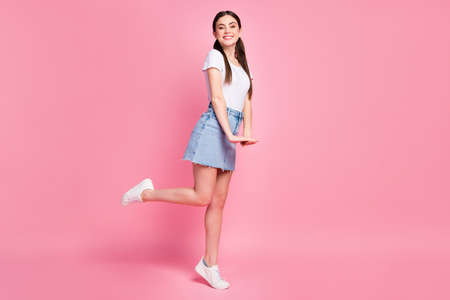 Full length profile photo of pretty cheerful lady street look outfit flirty mood wear casual white t-shirt mini denim skirt sneakers isolated pastel pink color backgroundの写真素材