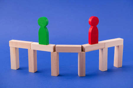 Two wooden figures friends leaders entrepreneurs businessmen standing on bridge gathering unity team building success understanding isolated over bright vivid shine vibrant blue color backgroundの写真素材
