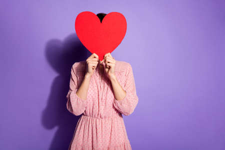 Portrait of charming lovely girl hide her face big red paper card heart, feel modest meet boyfriend...