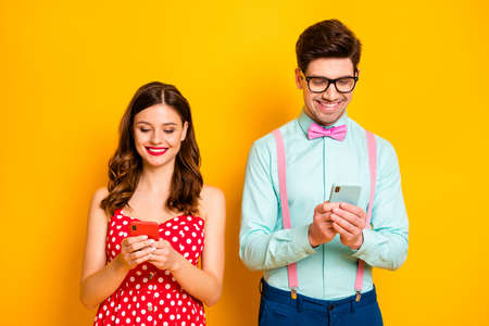 Photo of pretty lady handsome guy hold telephone browsing addicted users toothy smiling wear red dotted dress shirt bowtie isolated yellow bright color backgroundの写真素材