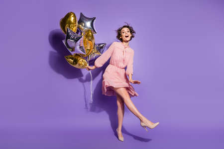 Full length photo of energetic candid girl hold many balloons enjoy prom graduation party wear polka-dot clothes footwear isolated over purple color backgroundの写真素材