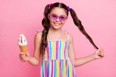 Photo of beautiful little lady two cute curly long tails hold big cone ice cream gelato weekend leisure wear cool sun specs colored summer dress isolated pastel pink color backgroundの写真素材